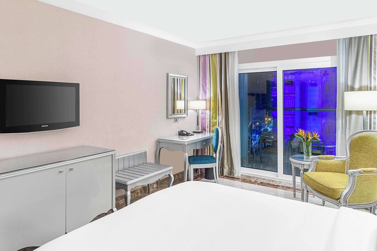 A hotel room with a bed, a desk, a chair, a television, and a window with a view of the city.