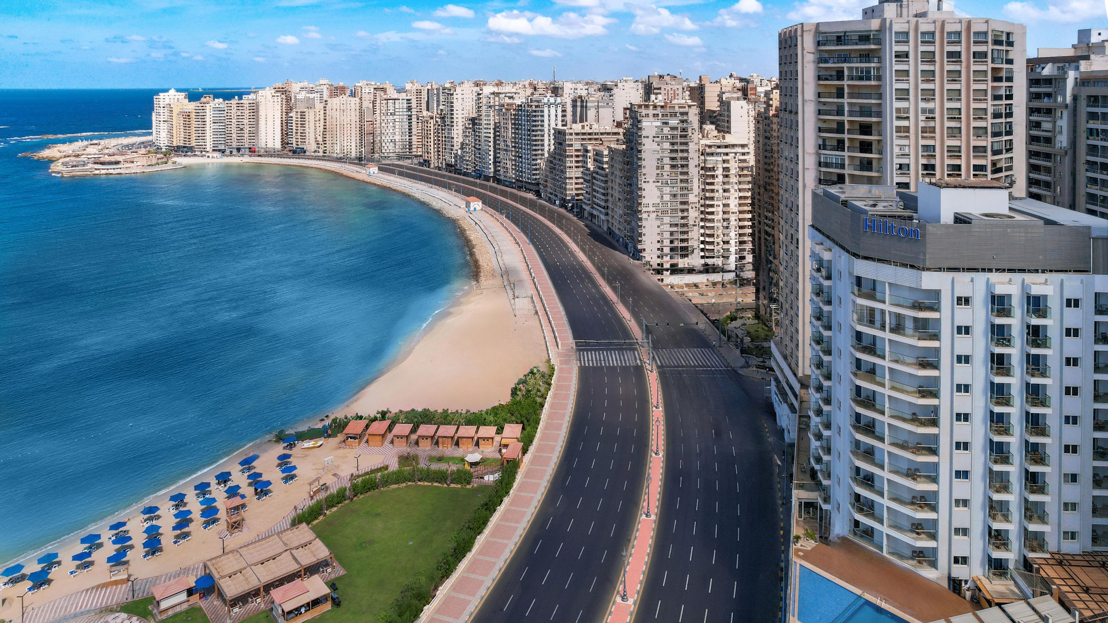 Un paisaje urbano costero con rascacielos, una playa y una carretera que serpentea a lo largo de la costa.
