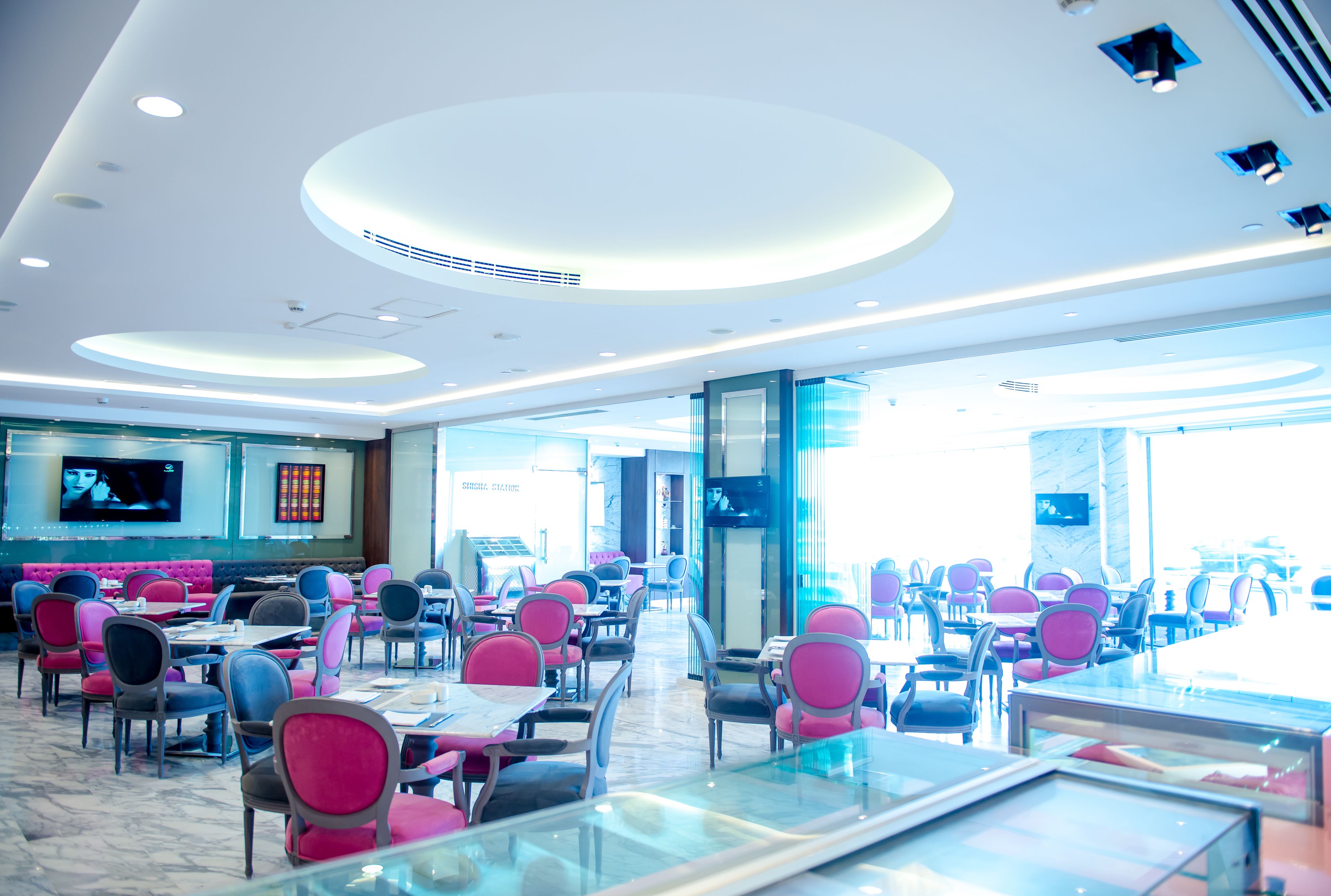 A spacious restaurant with multiple tables and chairs, a modern ceiling design, and large windows allowing natural light.