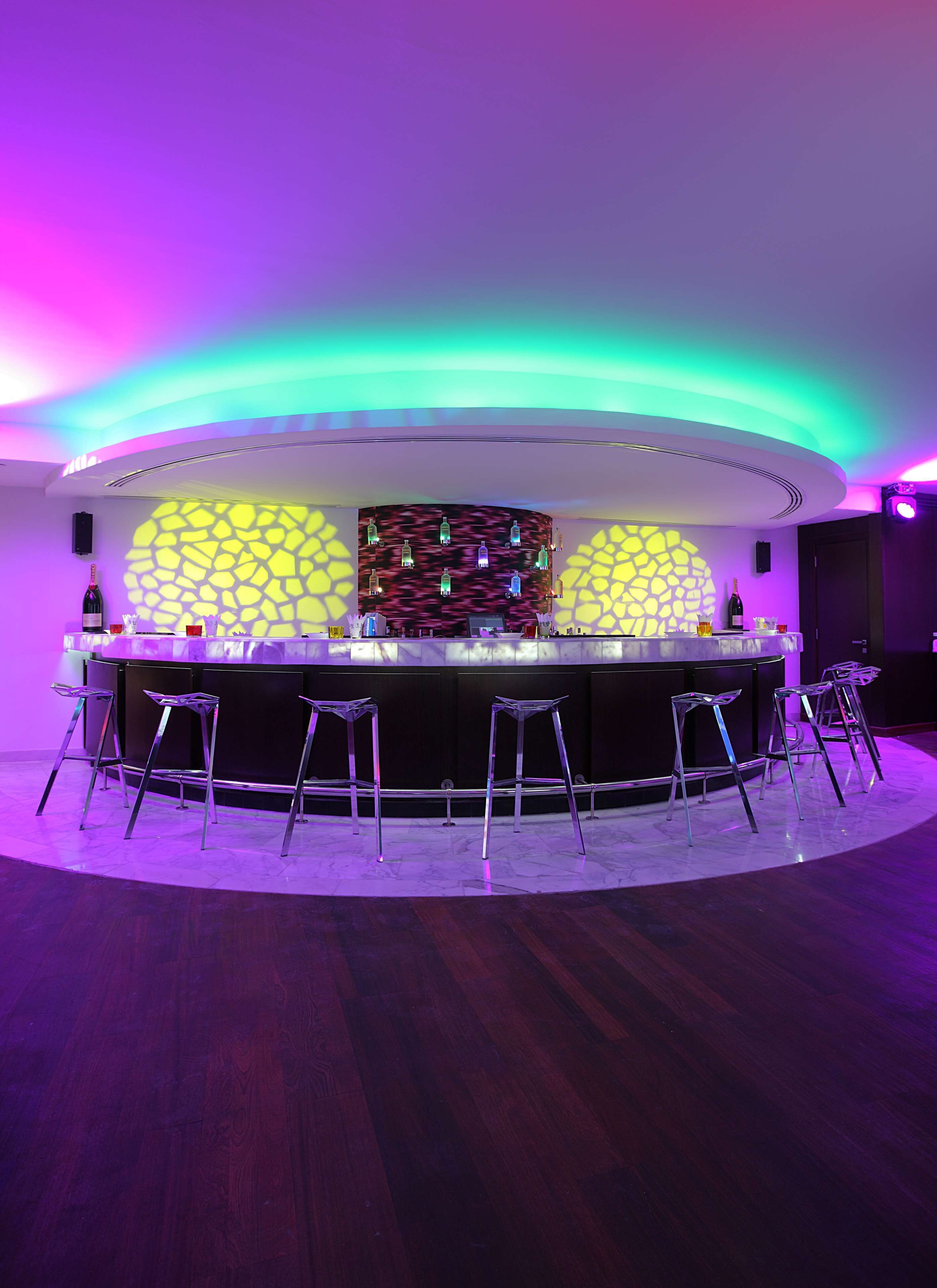 Un espace bar doté d’un comptoir circulaire, de tabourets de bar et d’un mur orné de motifs.