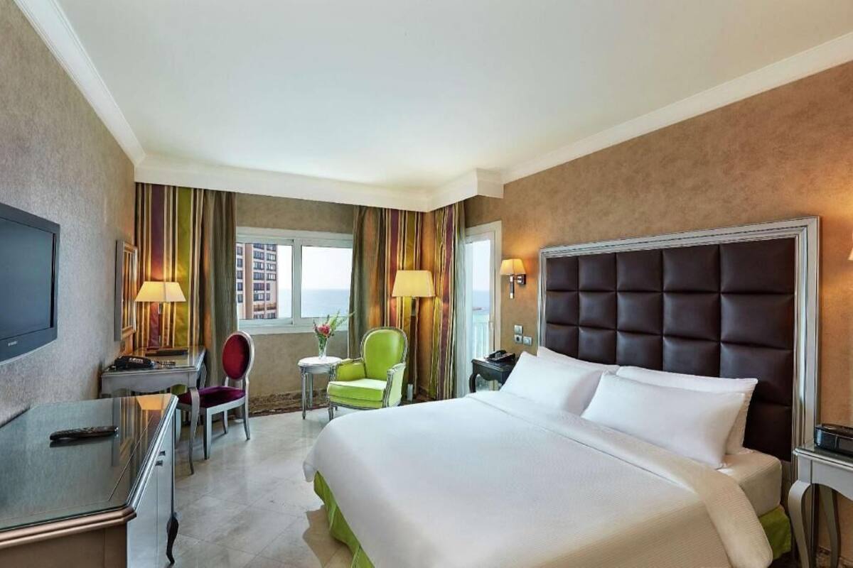 A hotel room with a bed, a desk, a chair, a TV, and a window.