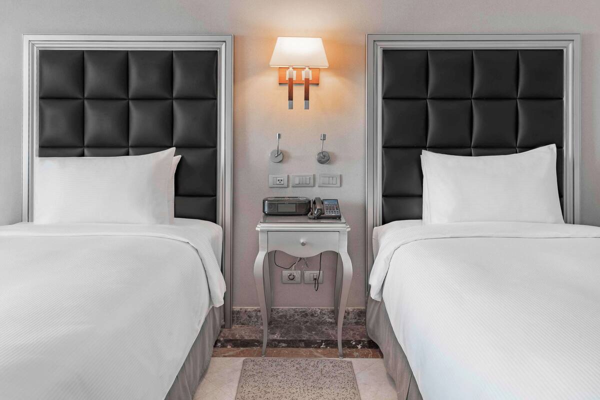 A hotel room with two beds, a nightstand, a lamp, and a telephone.