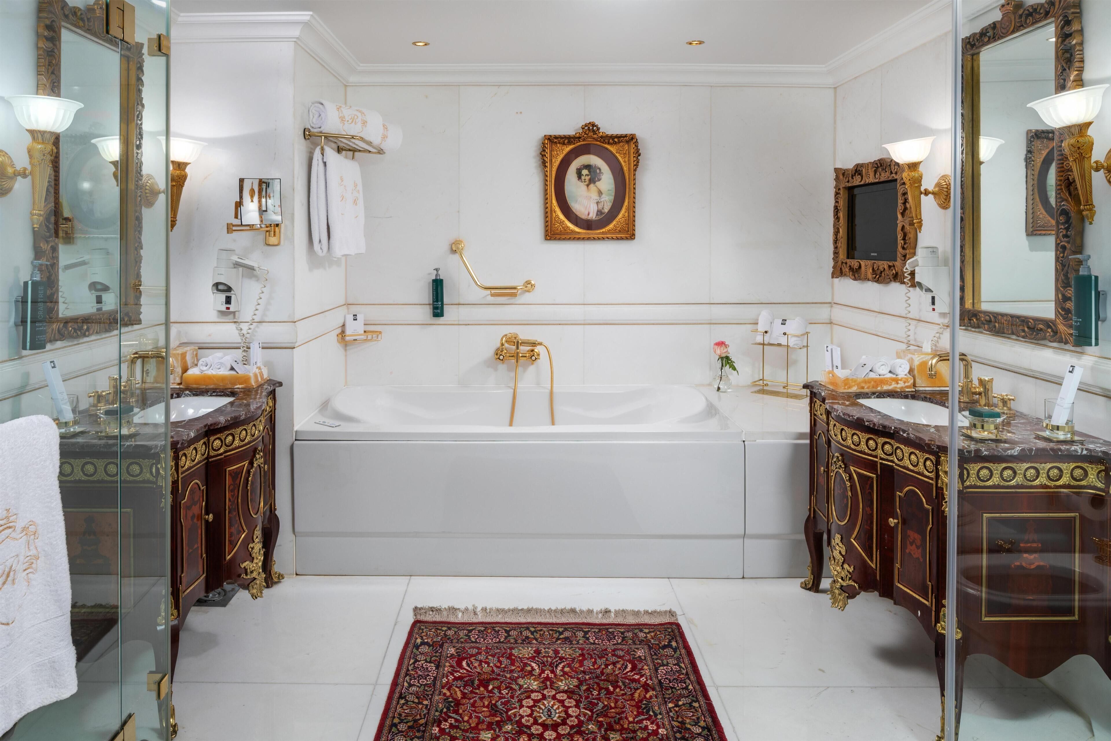 Un baño lujoso con una bañera grande, dos lavamanos decorados y un espejo con un marco ornamental.
