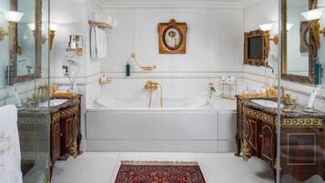 Een luxe badkamer met een groot bad, twee versierde wastafels en een spiegel met decoratieve lijst.