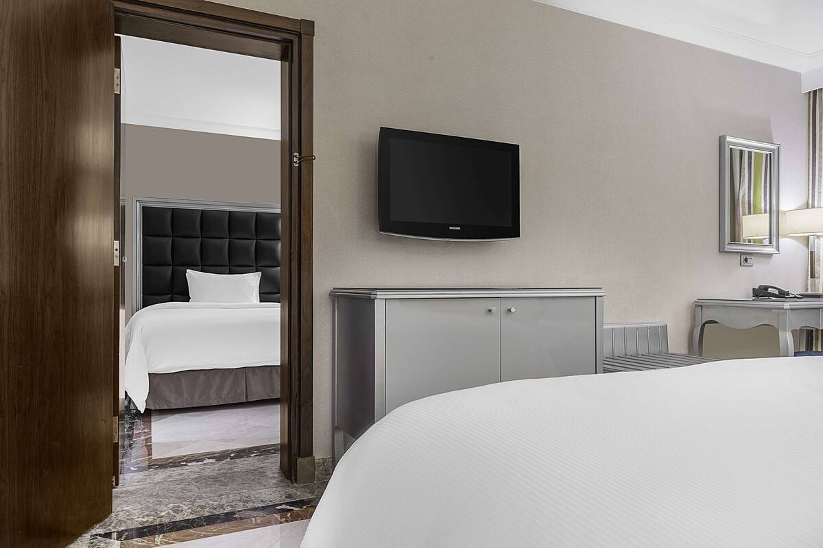 A hotel room with a bed, a television mounted on the wall, a bedside table, and a wardrobe.