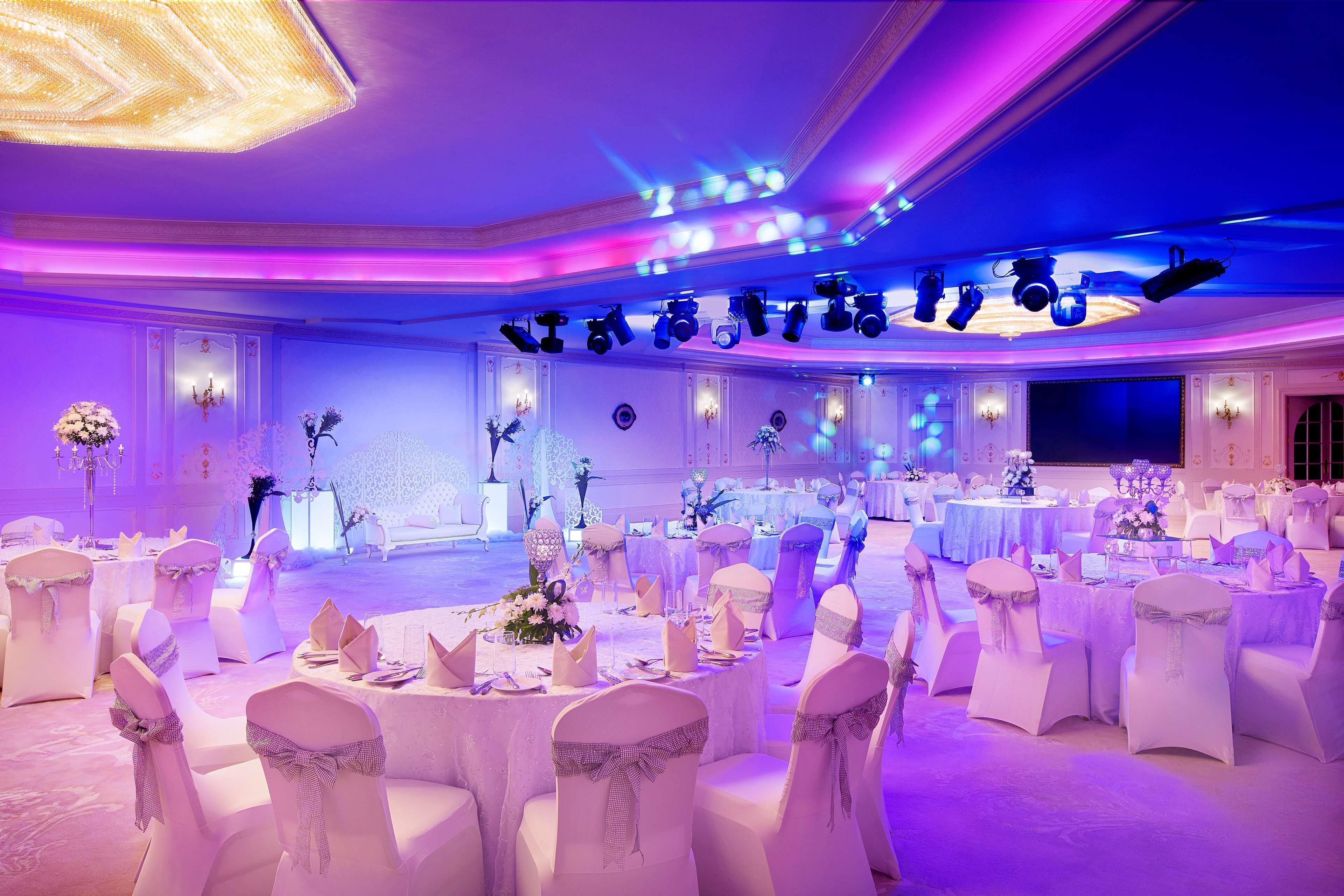 Un salón de banquetes con mesas redondas, sillas blancas y candelabros.