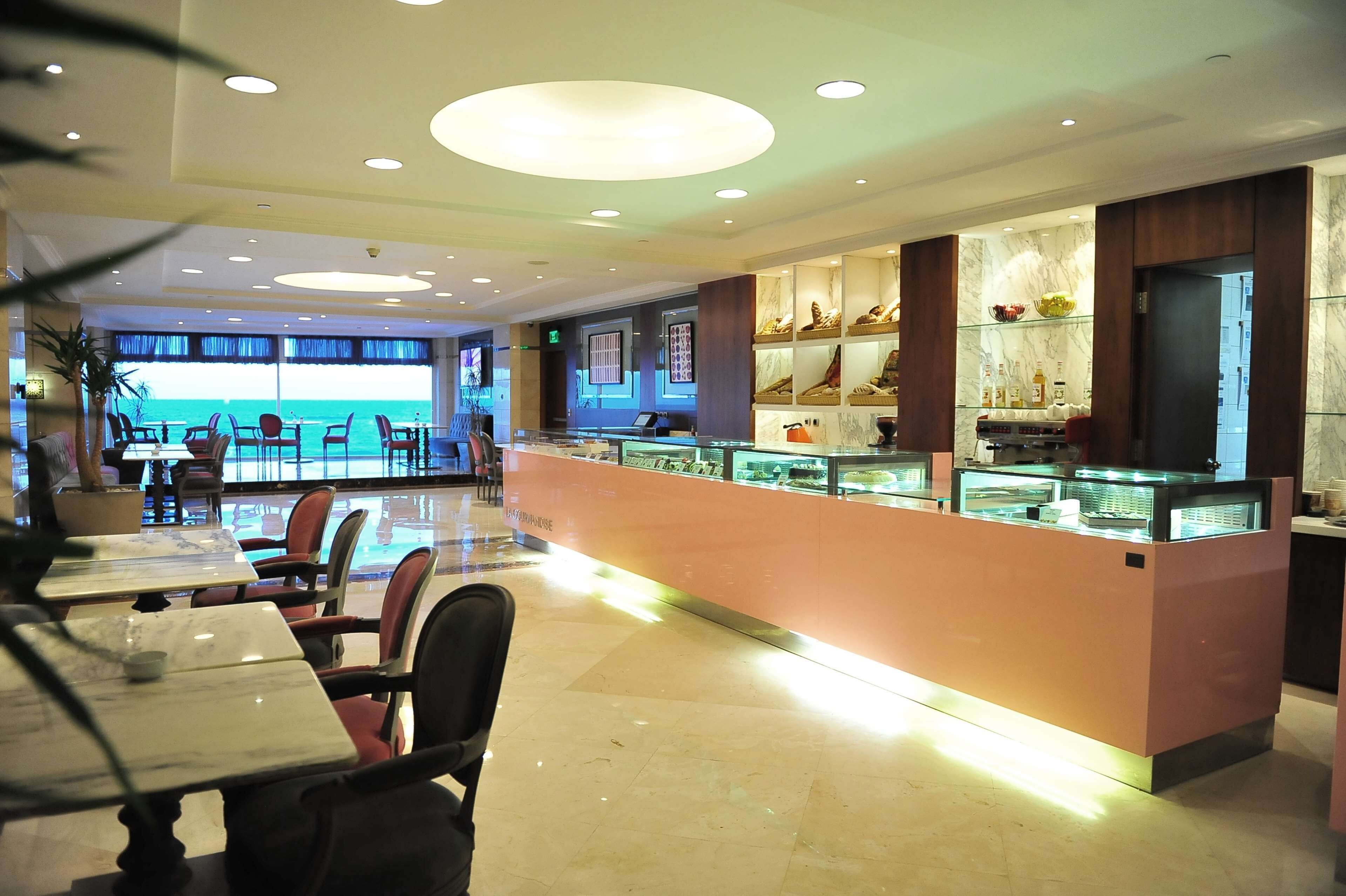 A modern hotel lobby with a central bar area, seating arrangements, and a view of the ocean.