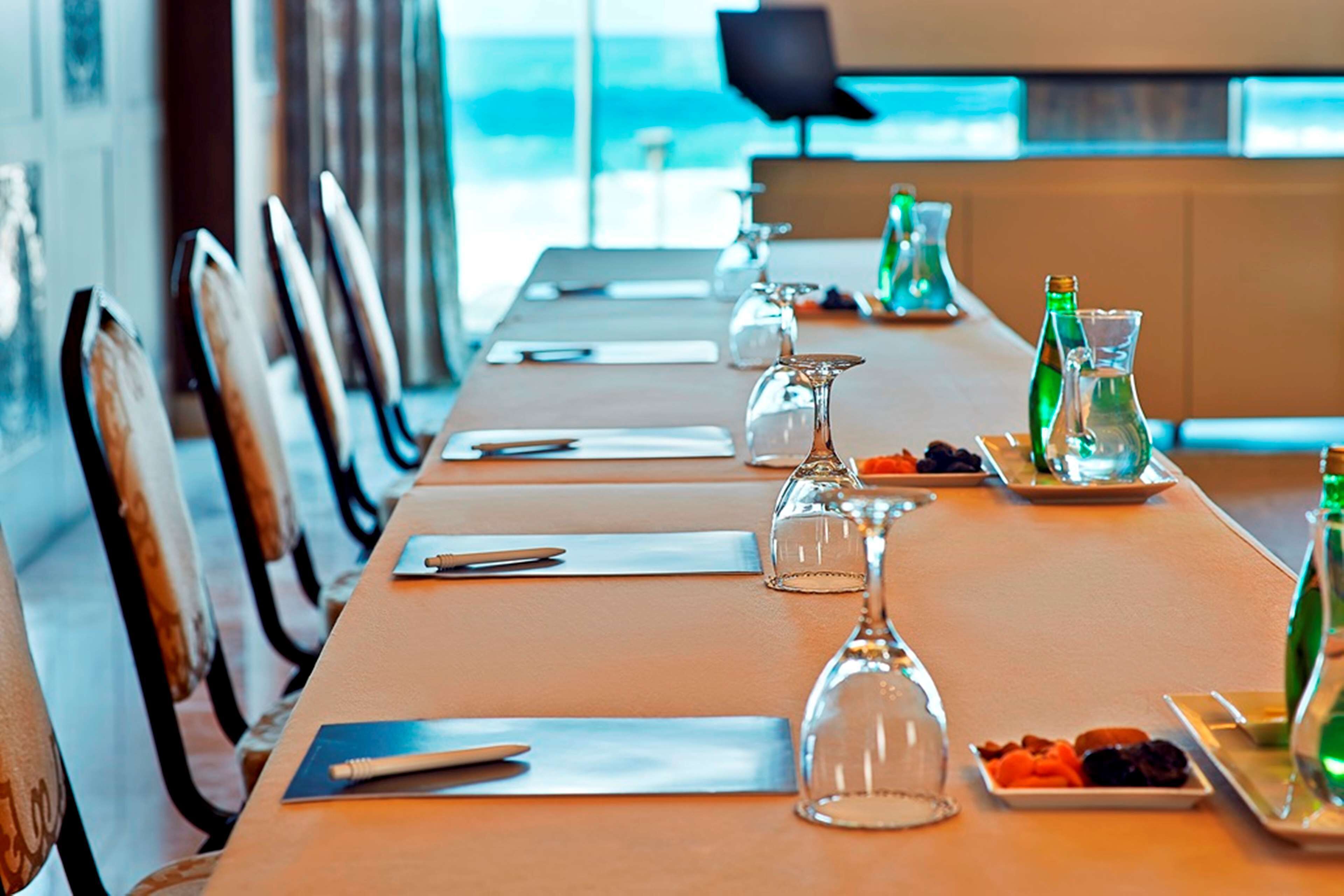 Una larga mesa de comedor dispuesta con platos, cubiertos, copas y botellas, con sillas a ambos lados.