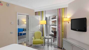 A hotel room with a bed, a green armchair, a small table, a TV, and a door leading to a balcony.