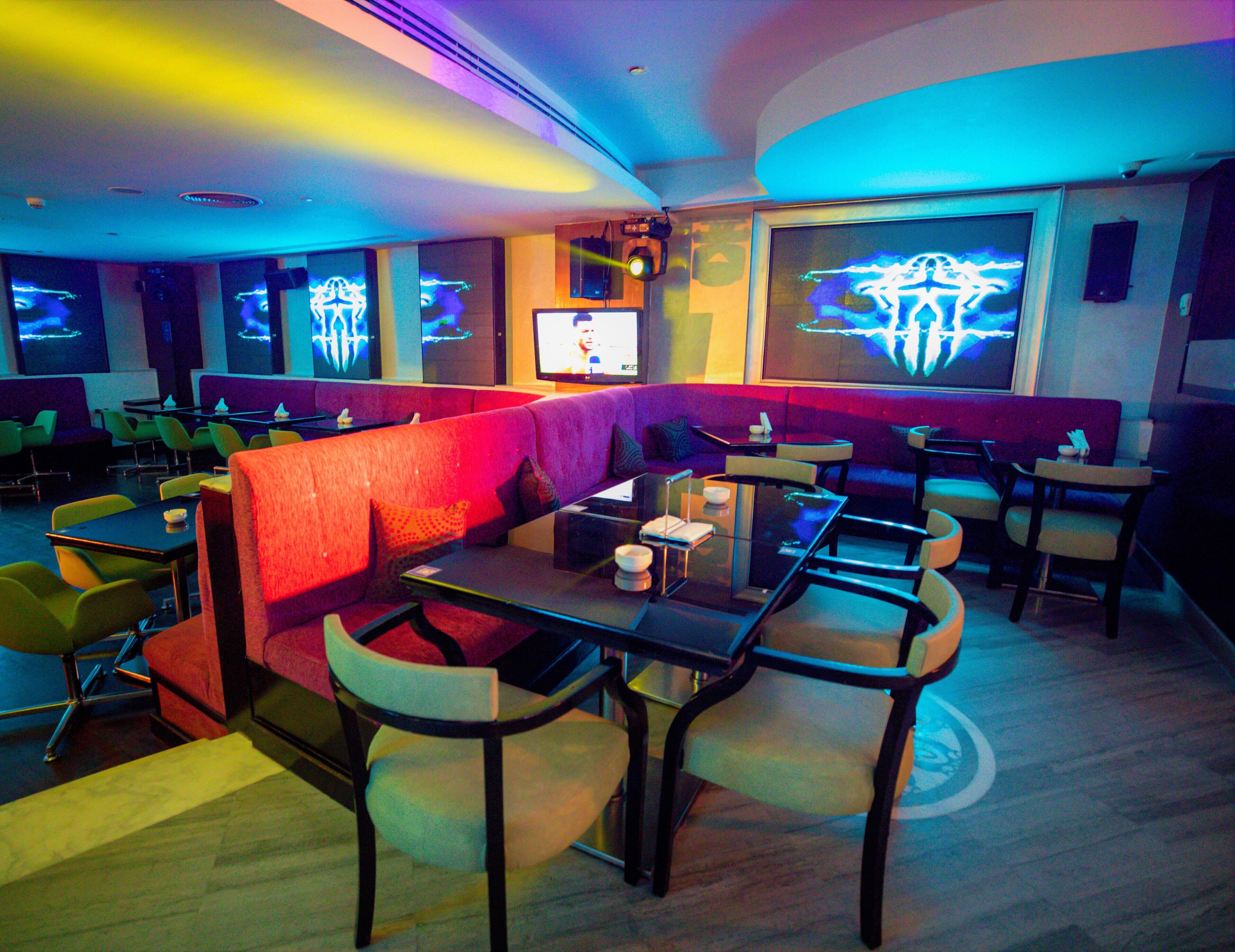 Un restaurante con cabinas y mesas, luces de neón y una pantalla de televisión.