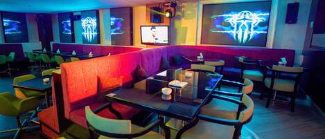 Un restaurante con cabinas y mesas, luces de neón y una pantalla de televisión.