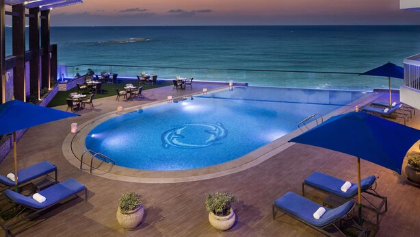 A pool area with lounge chairs and umbrellas, overlooking the ocean at dusk. - Hilton Alexandria Corniche (Alexandria)