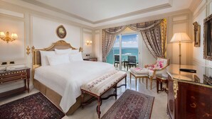 A luxurious bedroom with a large bed, a view of the sea, a sitting area with a chair and table, and elegant decor.