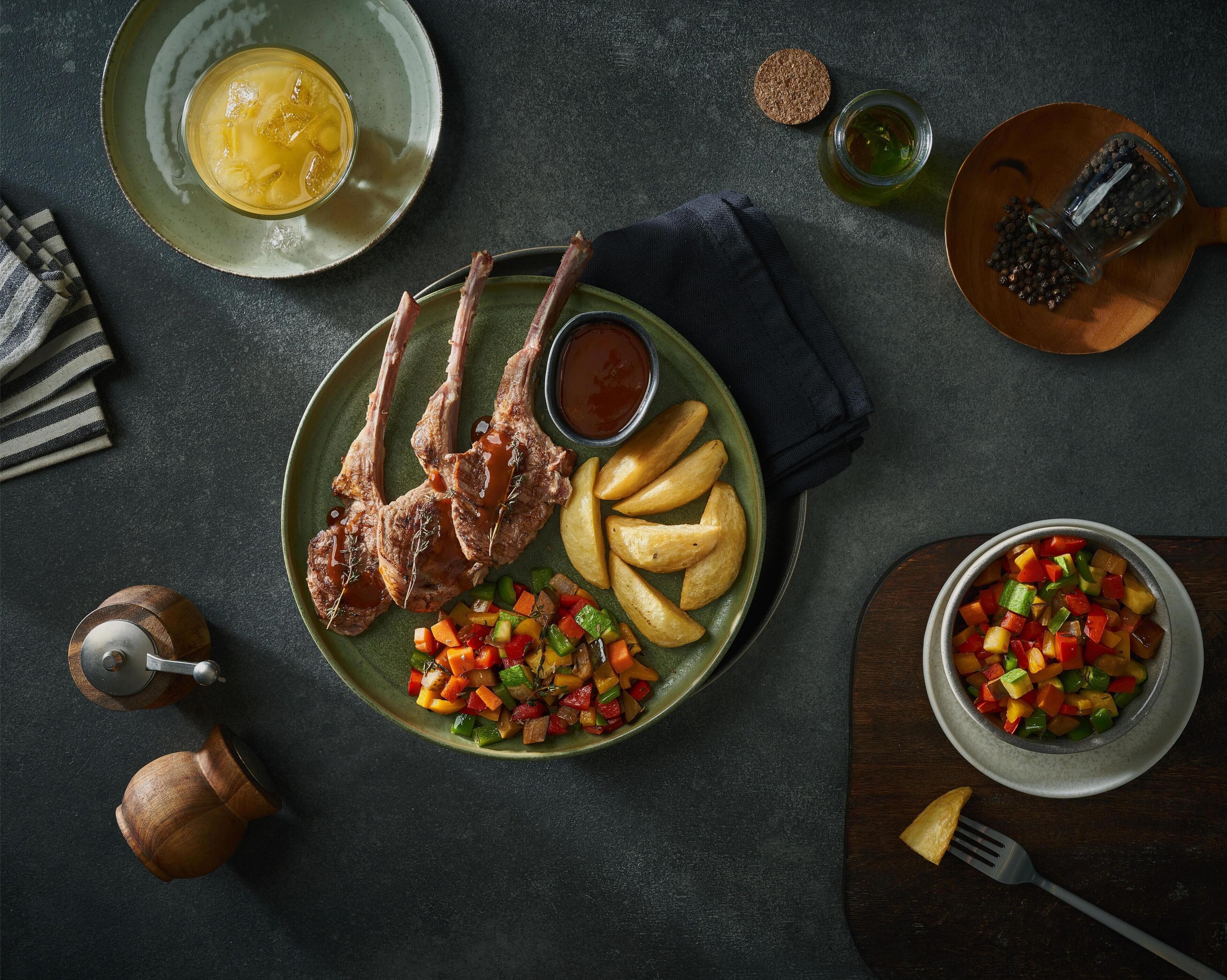 A plate with lamb chops, roasted potatoes, and a vegetable medley.