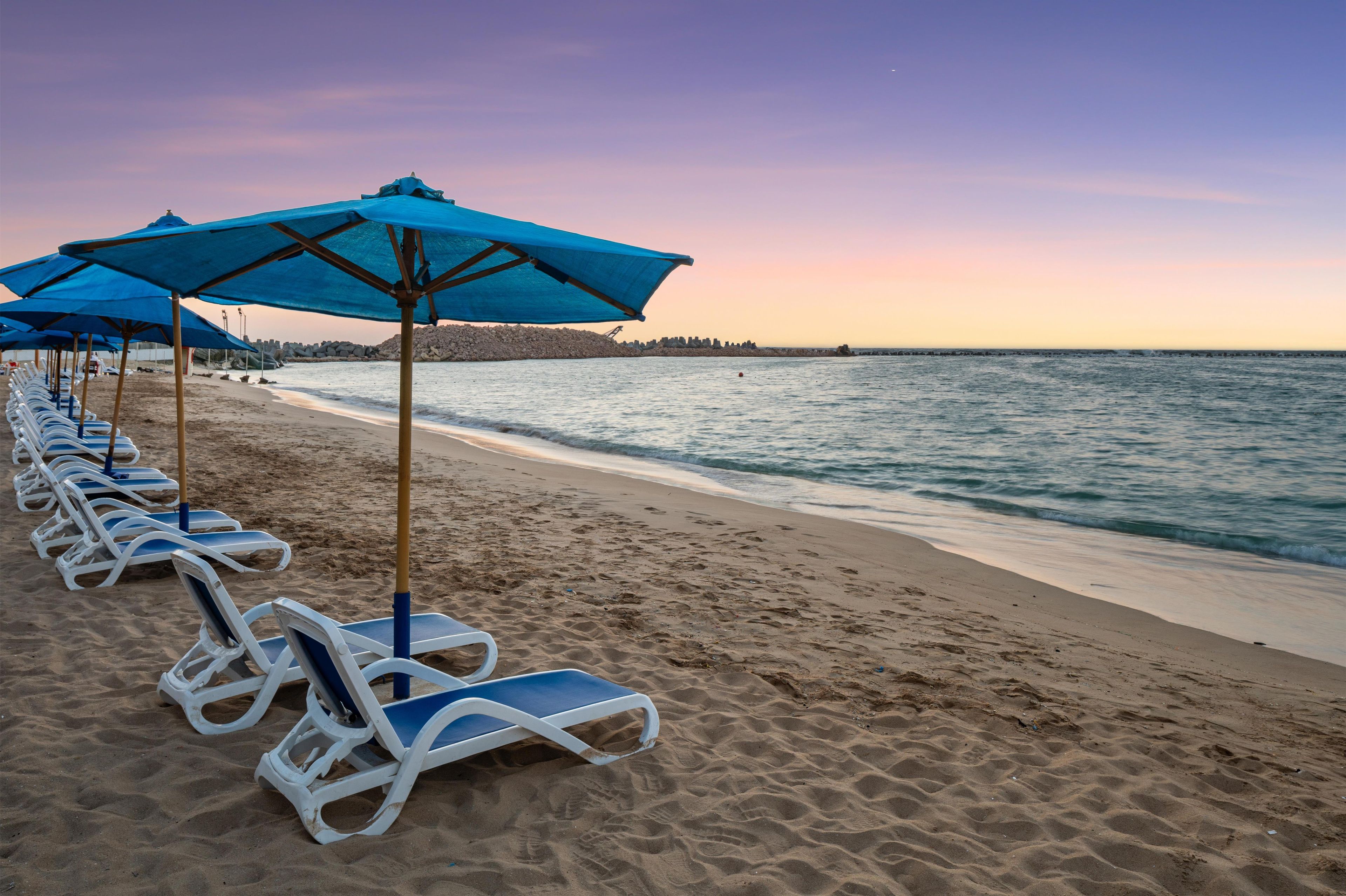 A beach with rows of sun loungers and blue umbrellas.