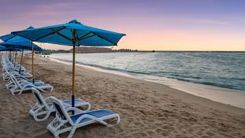 A beach with rows of sun loungers and blue umbrellas.