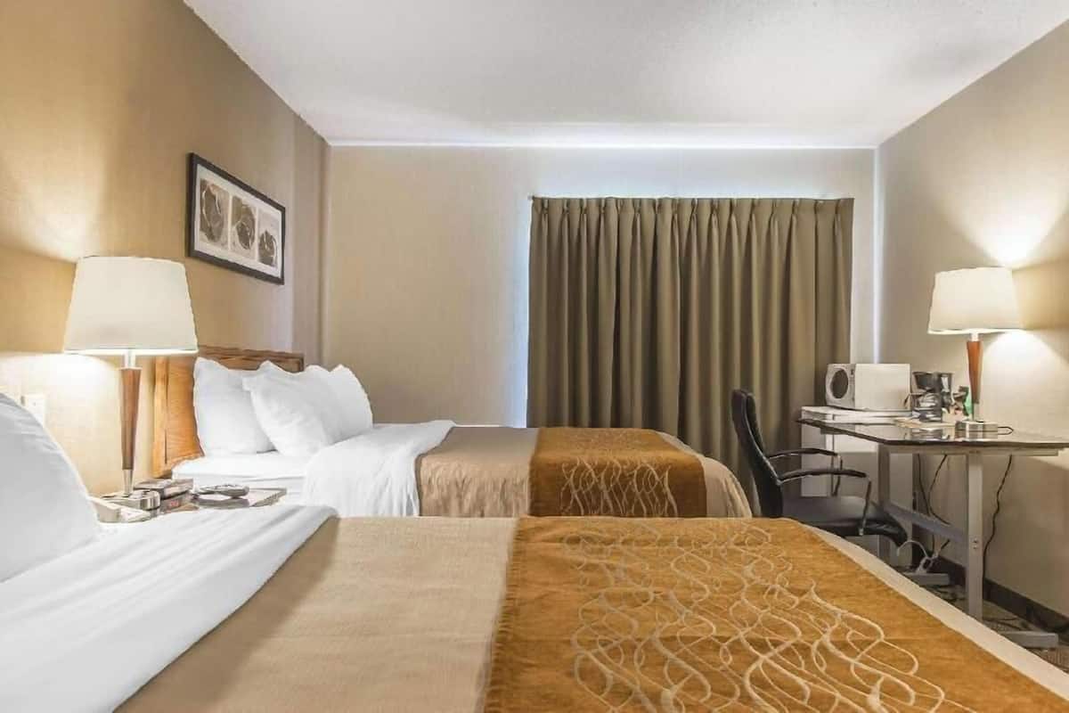 A hotel room with two beds, a desk, a chair, a lamp, and a window with curtains.