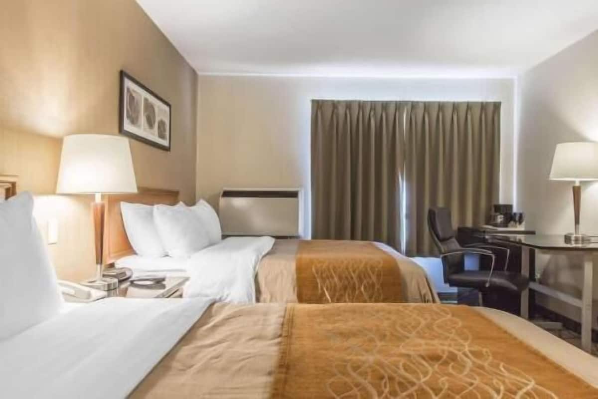 A hotel room with two beds, a desk, a chair, a lamp, and a window with curtains.
