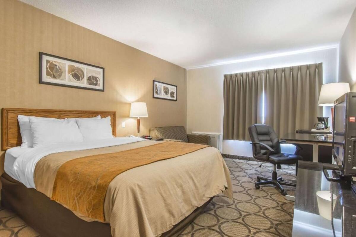 A hotel room with a bed, desk, chair, and a window with curtains.