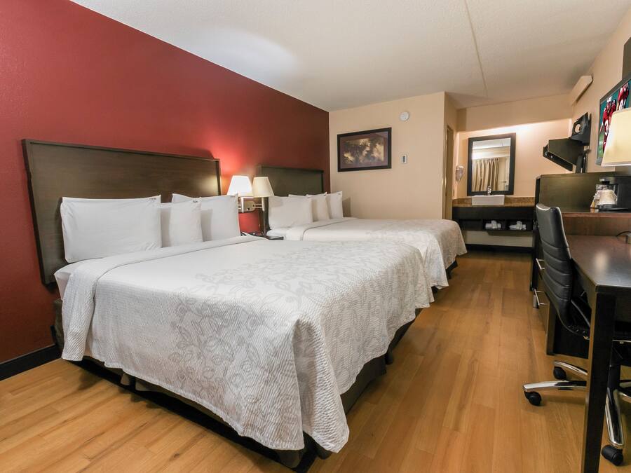 A hotel room with two beds, a desk, a chair, a lamp, and a mirror.