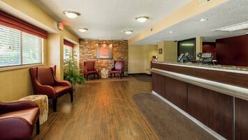 A reception area with a wooden floor, leather chairs, a stone wall, and a reception desk with a computer and phone.
