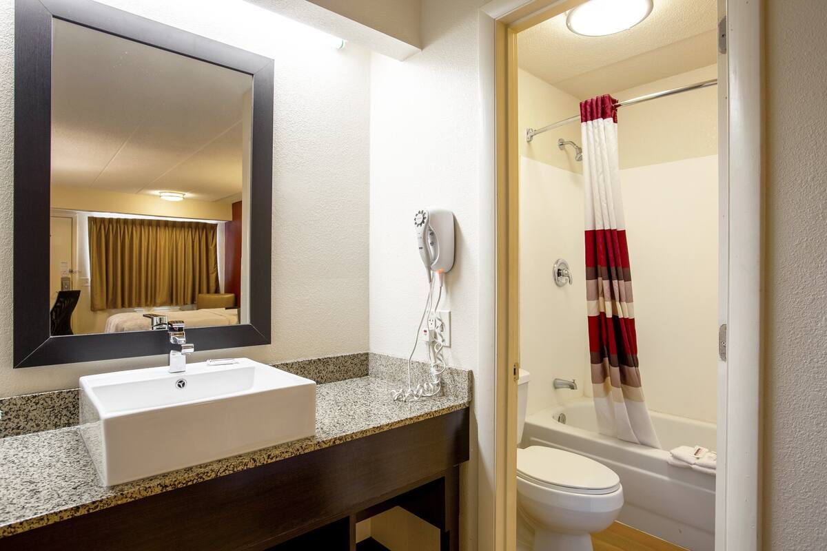 A bathroom with a sink, mirror, hairdryer, and shower curtain.
