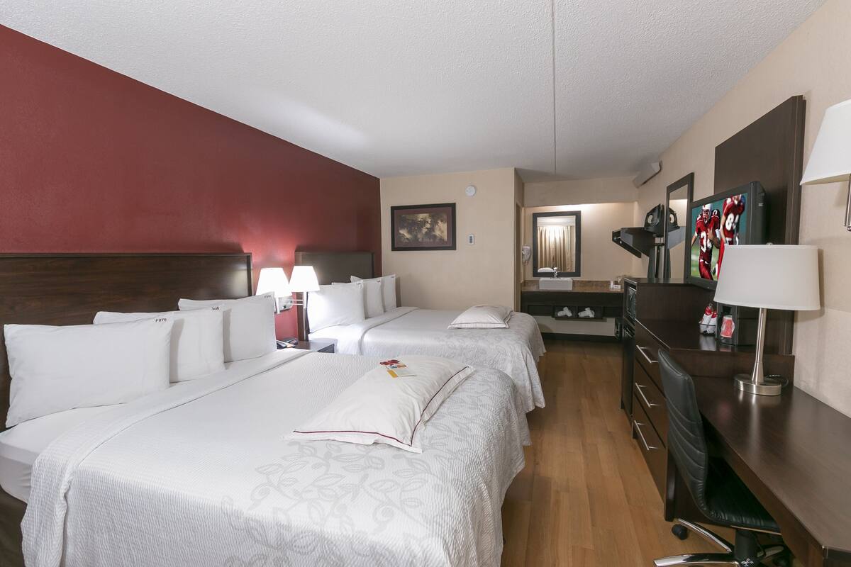 A hotel room with two beds, a desk, a chair, a lamp, and a mirror.