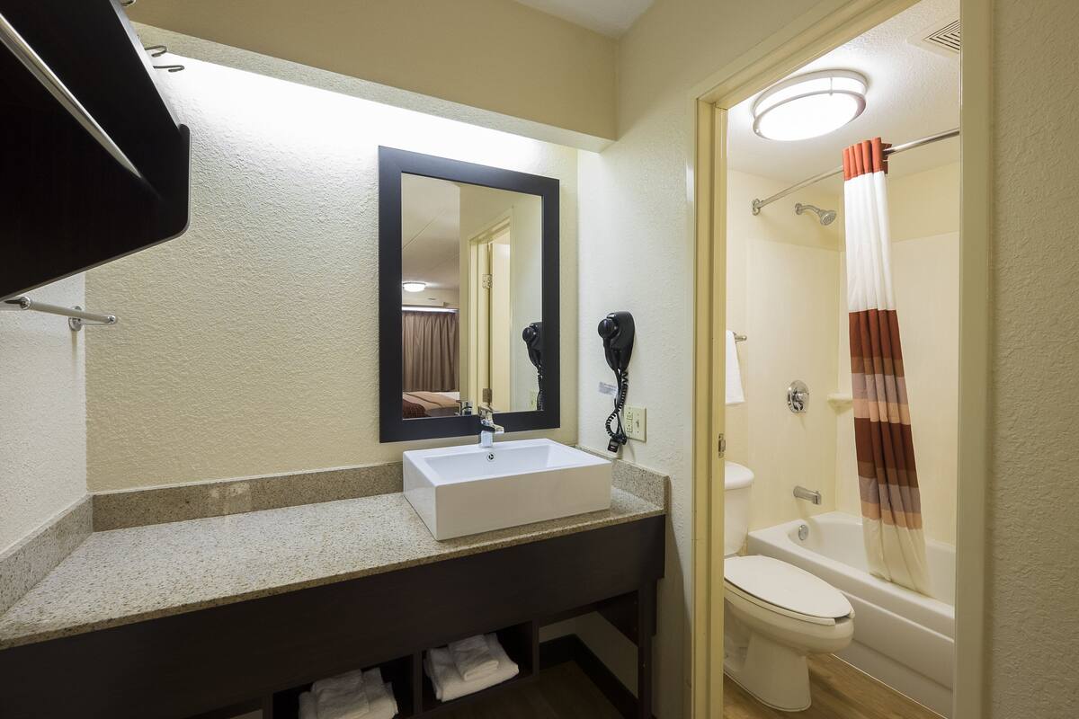 A bathroom with a white sink, a mirror, a toilet, and a shower with a striped curtain.