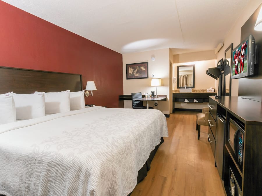 Quarto de hotel com cama grande, escrivaninha, cadeira, televisão e cozinha compacta.