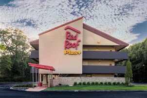 Un hotel Red Roof Plus con un diseño moderno, que presenta una señalización llamativa, una entrada cubierta y un jardín delantero ajardinado.