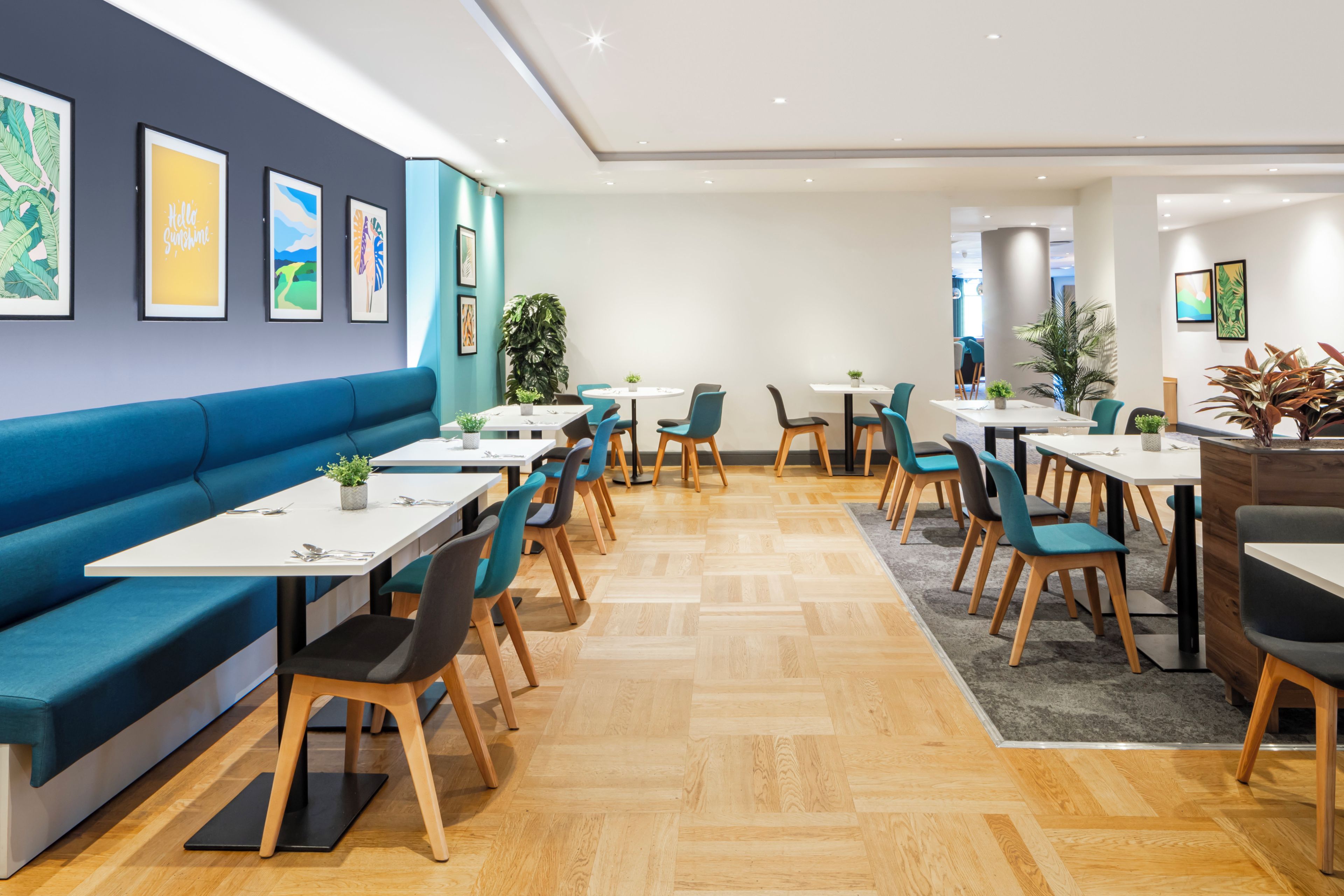 A modern dining area with a blue sofa, multiple tables, and chairs, and artwork on the walls.