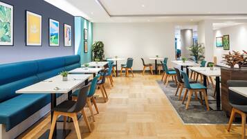 Un comedor moderno con un sofá azul, varias mesas y sillas, y obras de arte en las paredes.