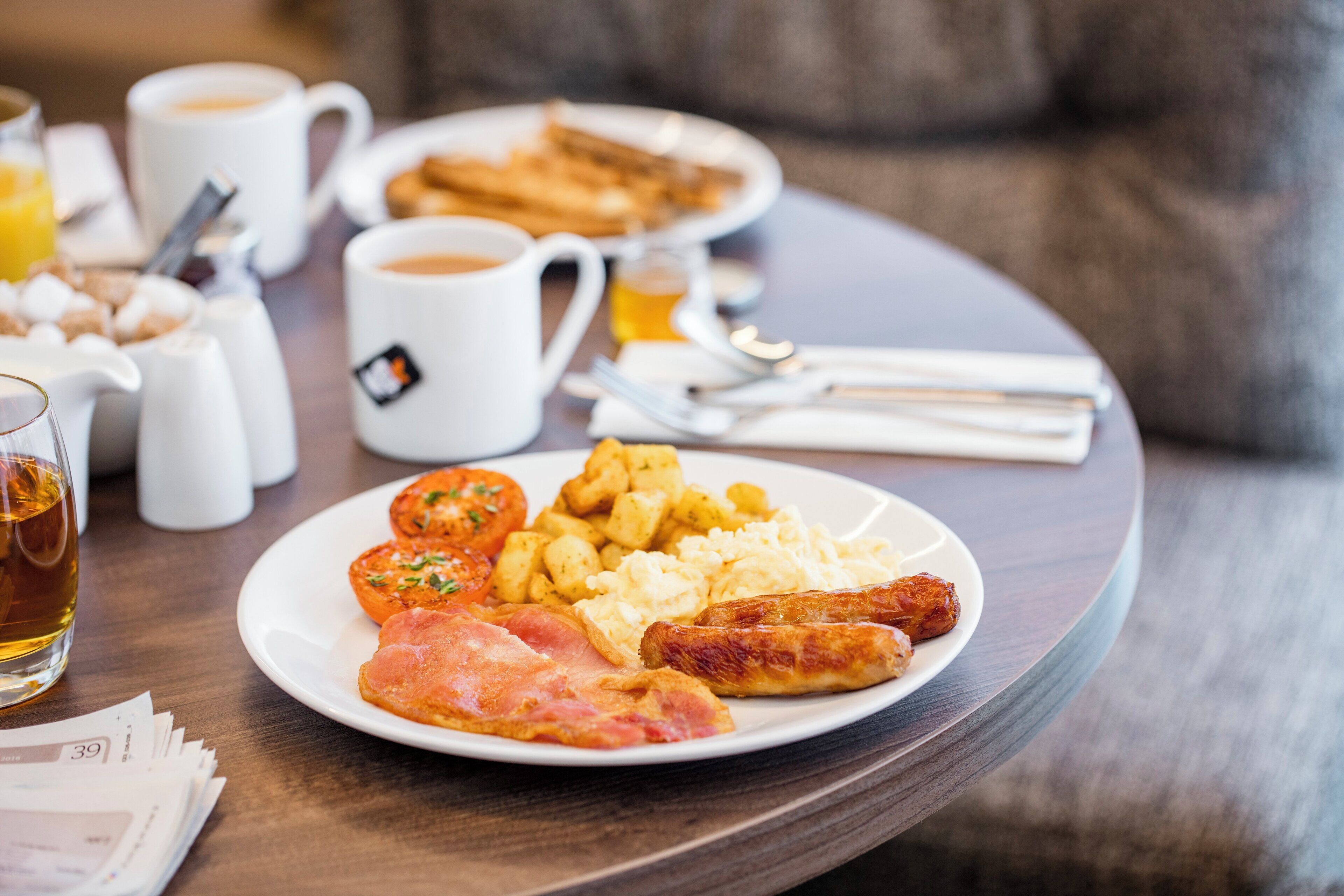 Ein Frühstückstisch mit Eiern, Würstchen und Schinken, dazu Kaffee und Saft.
