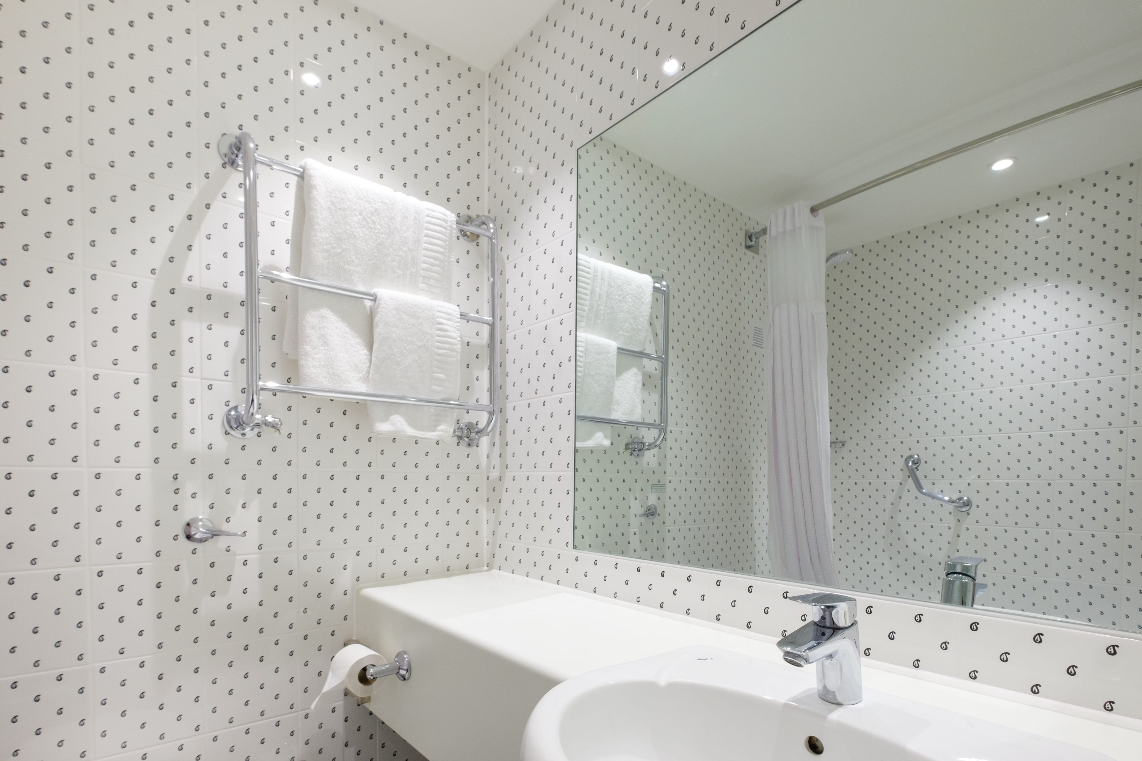 Un baño con lavamanos blanco, espejo y perchero.