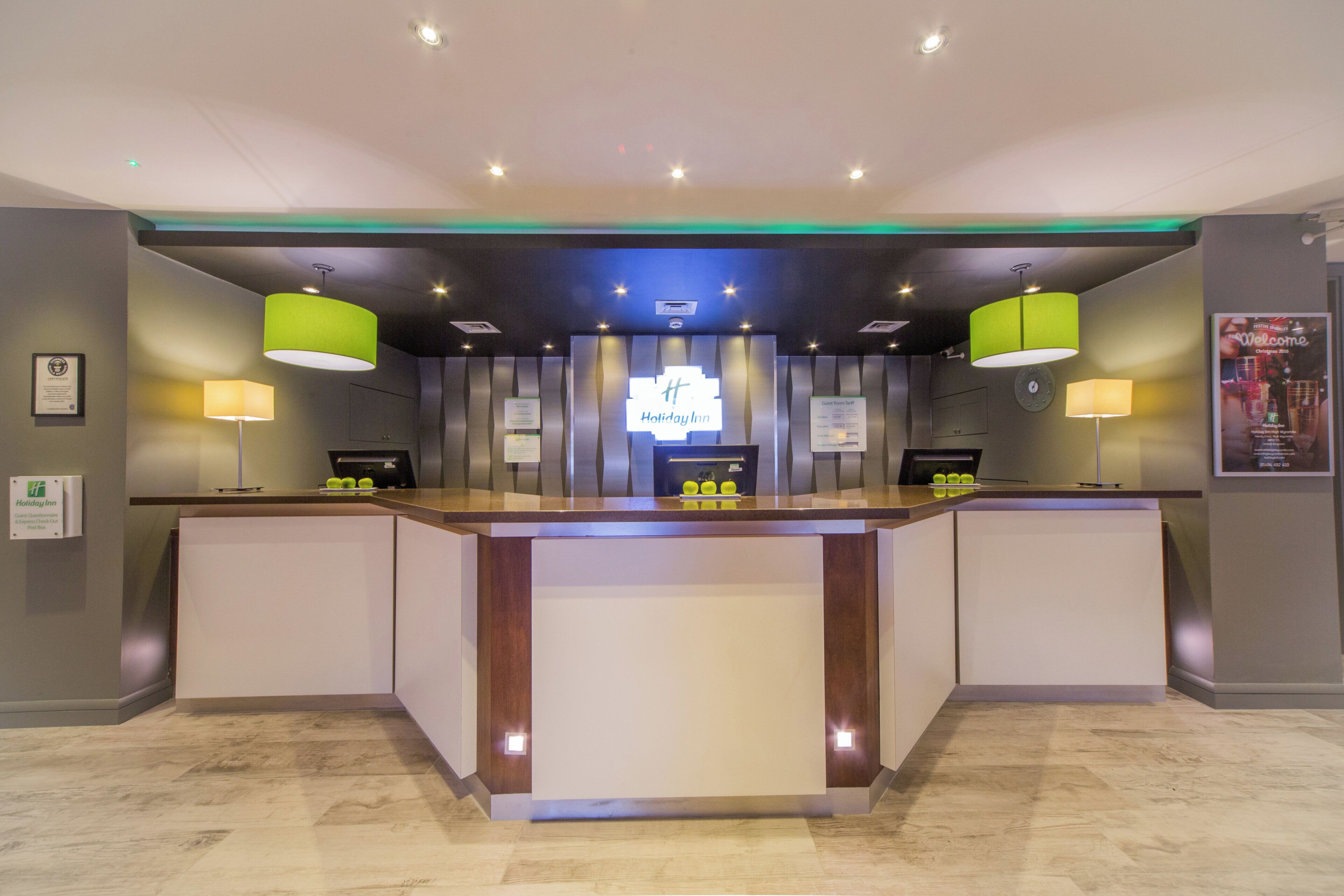 A reception desk with a 'Holiday Inn' sign, a guest room tariff, and a 'Welcome' poster.