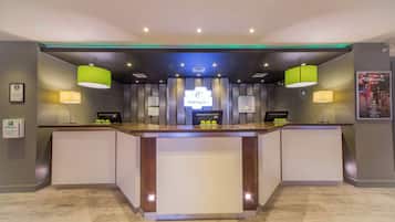 A reception desk with a 'Holiday Inn' sign, a guest room tariff, and a 'Welcome' poster.