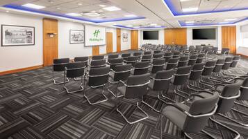 A conference room with rows of chairs, a large screen, and a Holiday Inn sign.