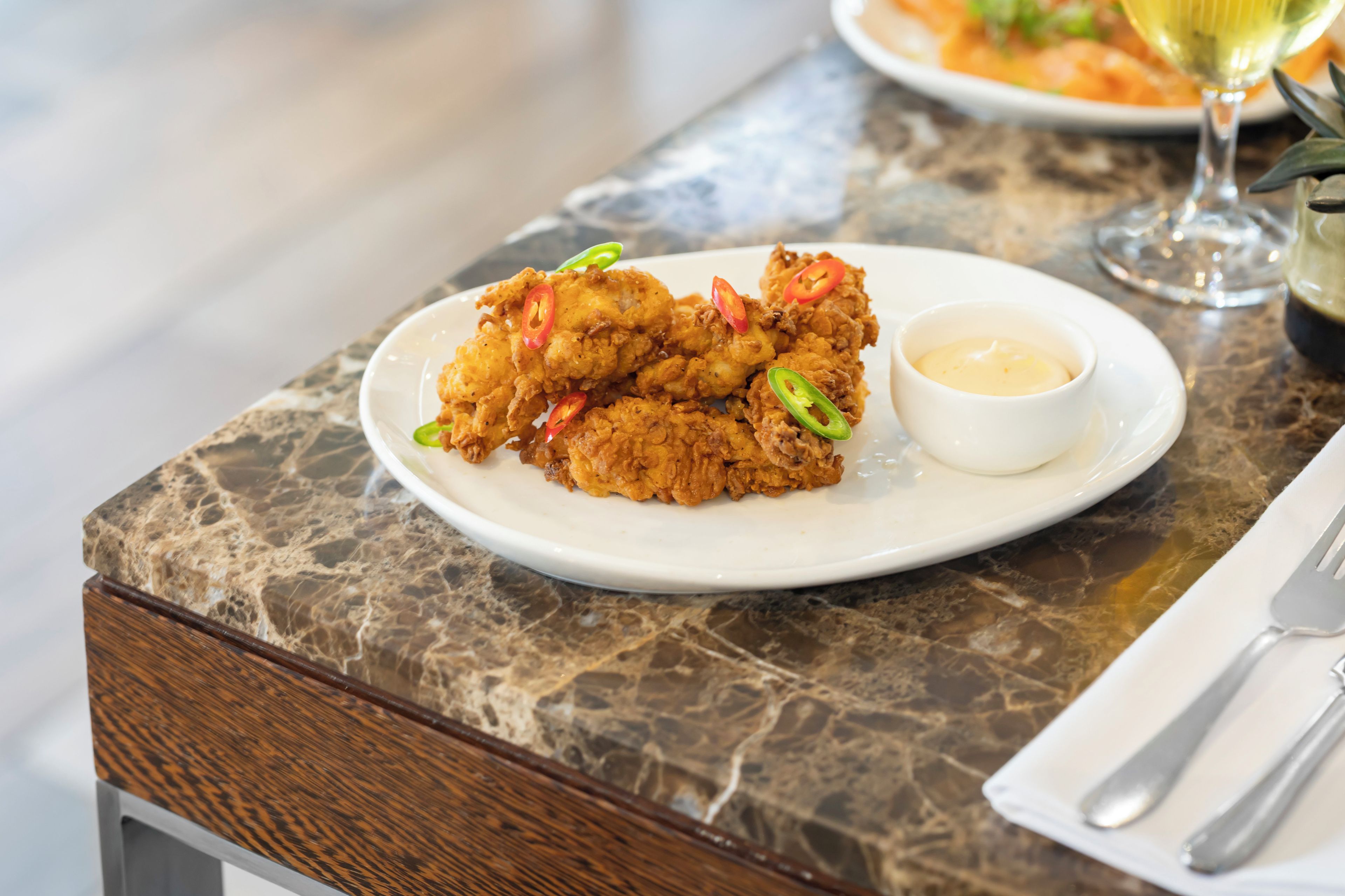 Un plato de pollo frito con rodajas de jalapeño sobre una encimera de mármol.