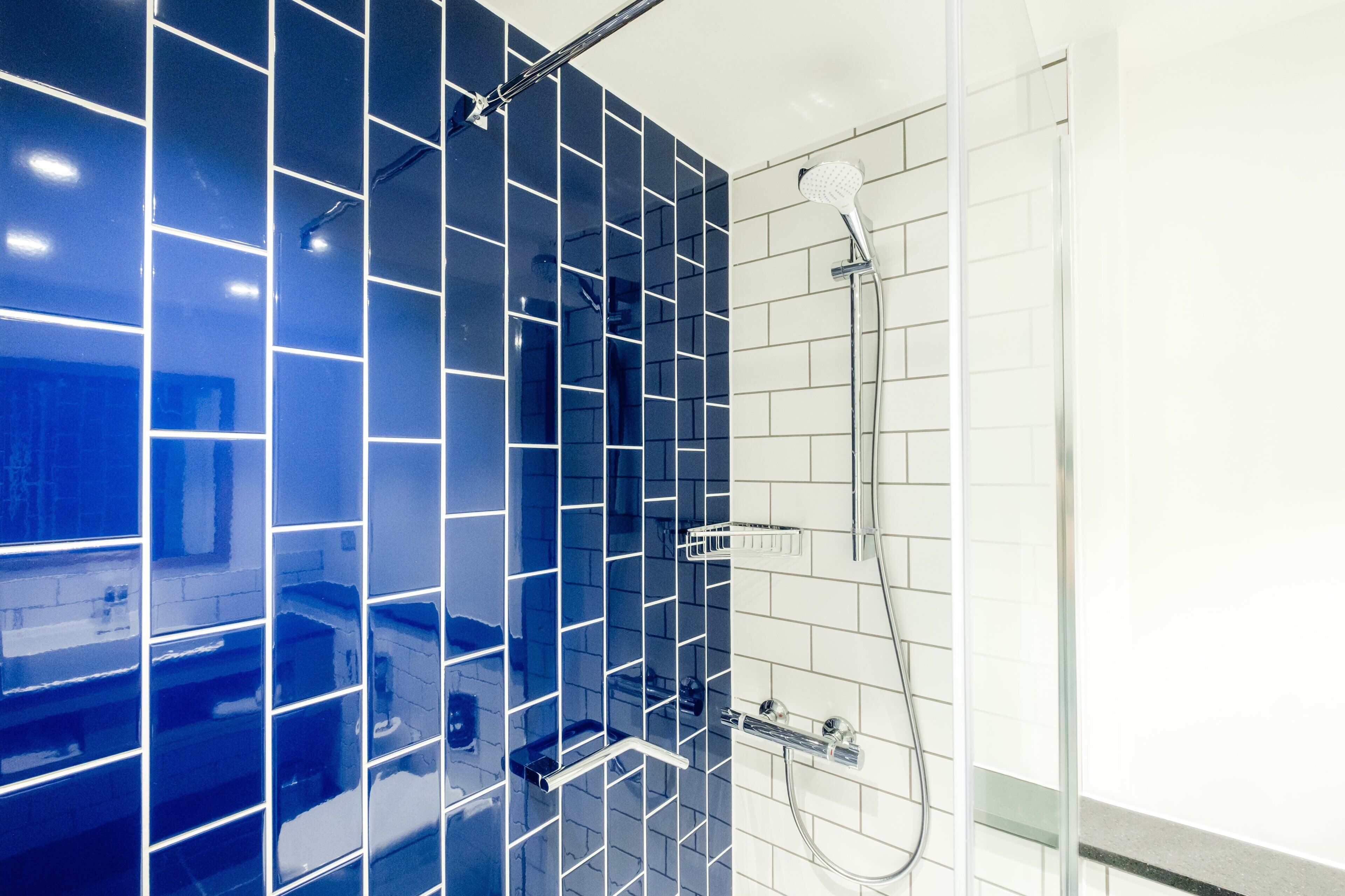 Une salle de bain avec un mur de douche recouvert de carreaux bleus et une zone de douche recouverte de carreaux blancs.