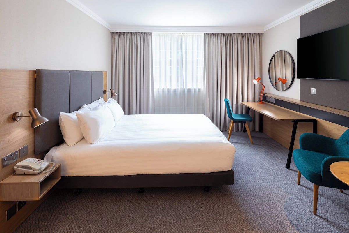 A hotel room with a large bed, a desk, a chair, a TV, and a telephone.