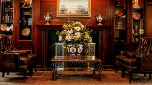 A formal room with a fireplace, leather chairs, a table with a vase of flowers, and wooden shelves with decorative items. - Olde Mill Inn (Basking Ridge)