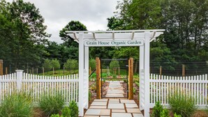 A garden entrance with a white picket fence, a stone pathway, and a sign reading "Grain House Organic Garden". - Olde Mill Inn (Basking Ridge)