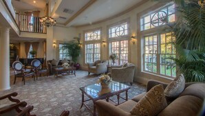 A spacious living room with a grand piano, comfortable seating, large windows, and a chandelier. - Olde Mill Inn (Basking Ridge)
