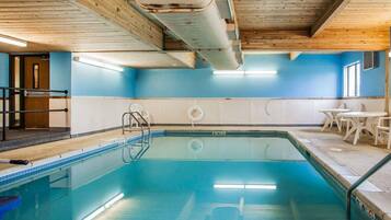 A swimming pool with a wooden ceiling, a blue wall, and a table with chairs.