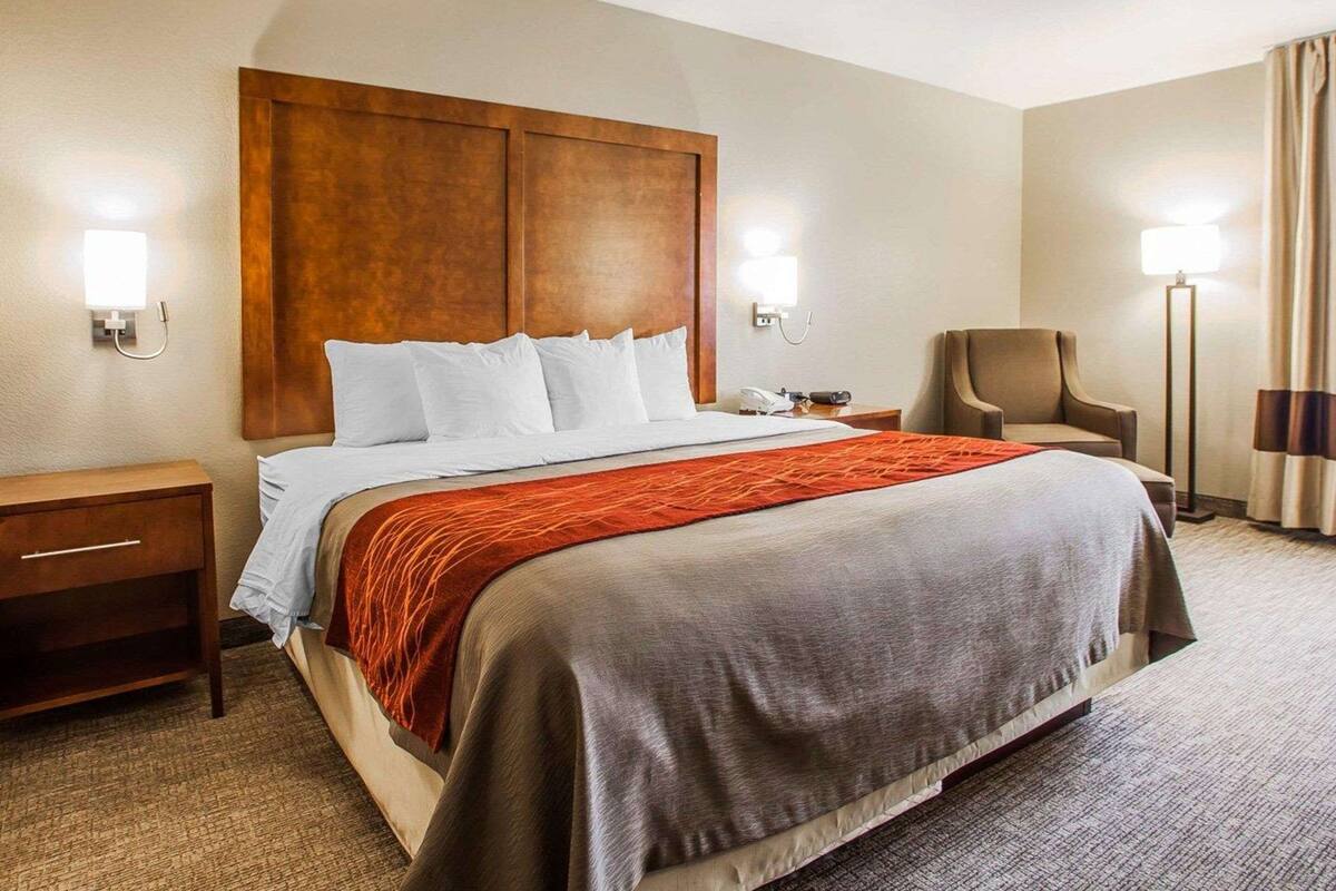 A hotel room with a large bed, a wooden headboard, two bedside tables, a chair, and a floor lamp.
