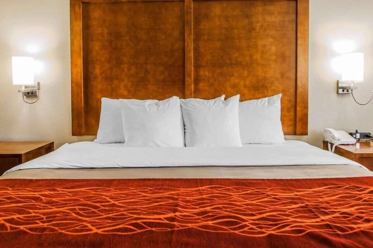 A hotel room with a large bed, two bedside tables, a wooden headboard, and wall-mounted lights.