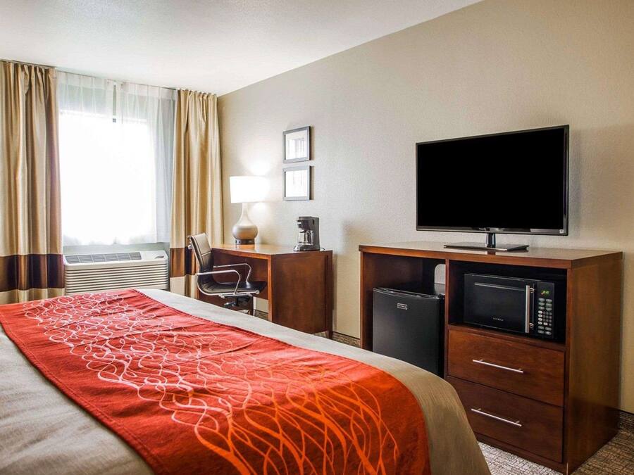A hotel room with a bed, a desk with a lamp, a television, a coffee maker, and a microwave.