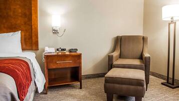 A hotel room with a bed, a nightstand with a lamp, a chair, and a carpeted floor.