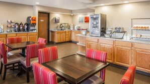 A hotel dining area with a buffet setup, wooden cabinets, and red upholstered chairs. - Comfort Inn Marshalltown South (Marshalltown)