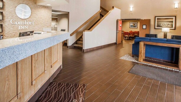 A hotel lobby with a reception desk, a staircase, seating area, and a wall-mounted sign. - Comfort Inn Marshalltown South (Marshalltown)